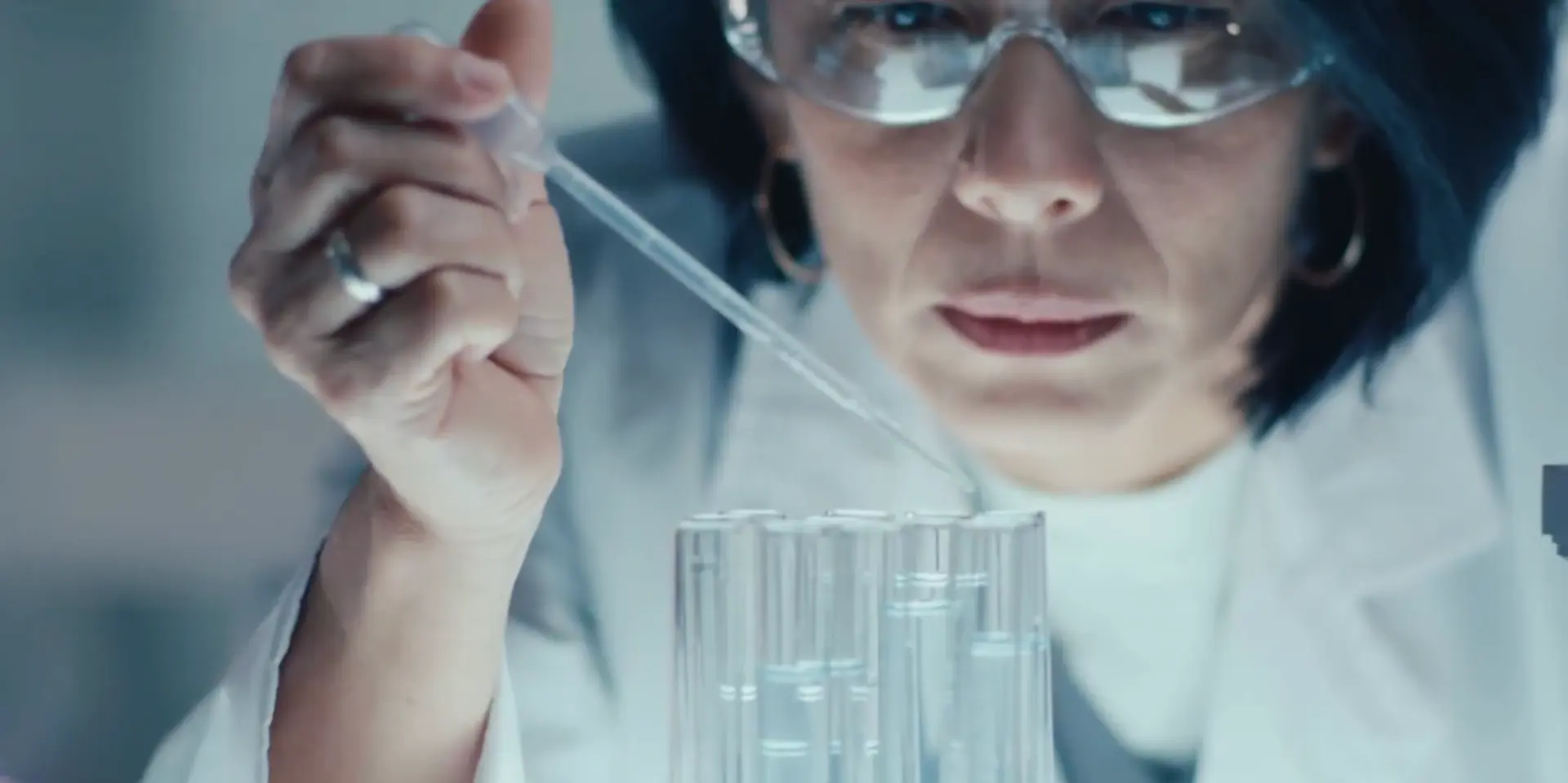 A scientist in safety glasses using a pipette with test tubes in a laboratory